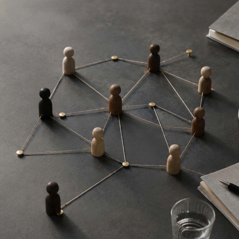 Wooden peg figures connected by strings and pins, forming a network on a desk to symbolize collaboration or social connections.