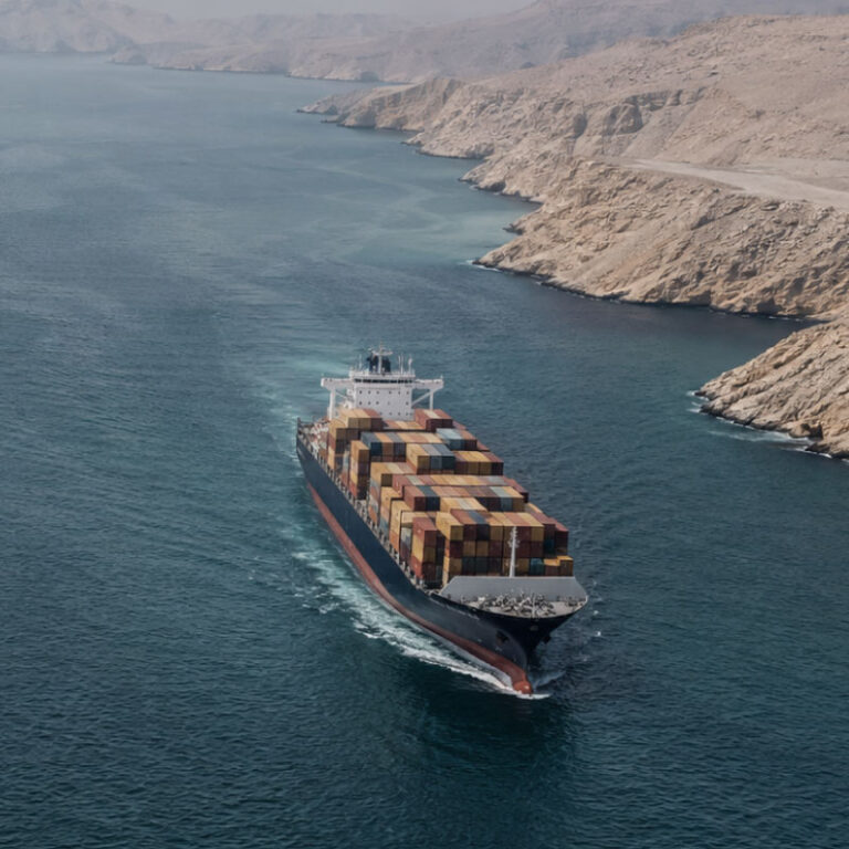 Container ship sailing through a narrow coastal passage lined with rugged beige cliffs, stacked colorful cargo containers on deck.