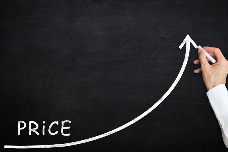 Hand drawing a white chalk curved arrow rising upward on a blackboard, illustrating price increase in a business context.
