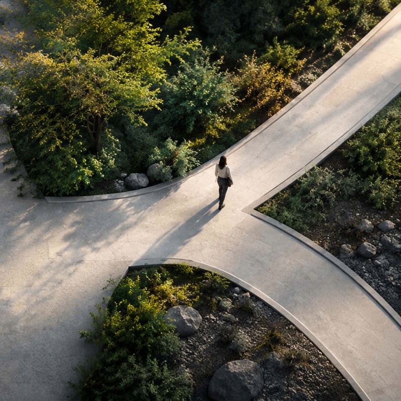 High-angle aerial view of a person walking along a curved pathway split by lush greenery, symbolizing conscious leadership choices and navigating organizational change